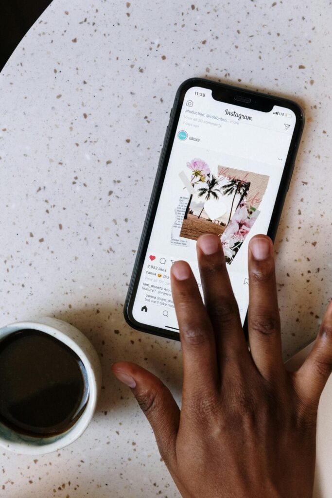 Person's hand holding a smartphone over a table, displaying an Instagram post featuring a photo collage with tropical plants and travel images, next to a cup of coffee.