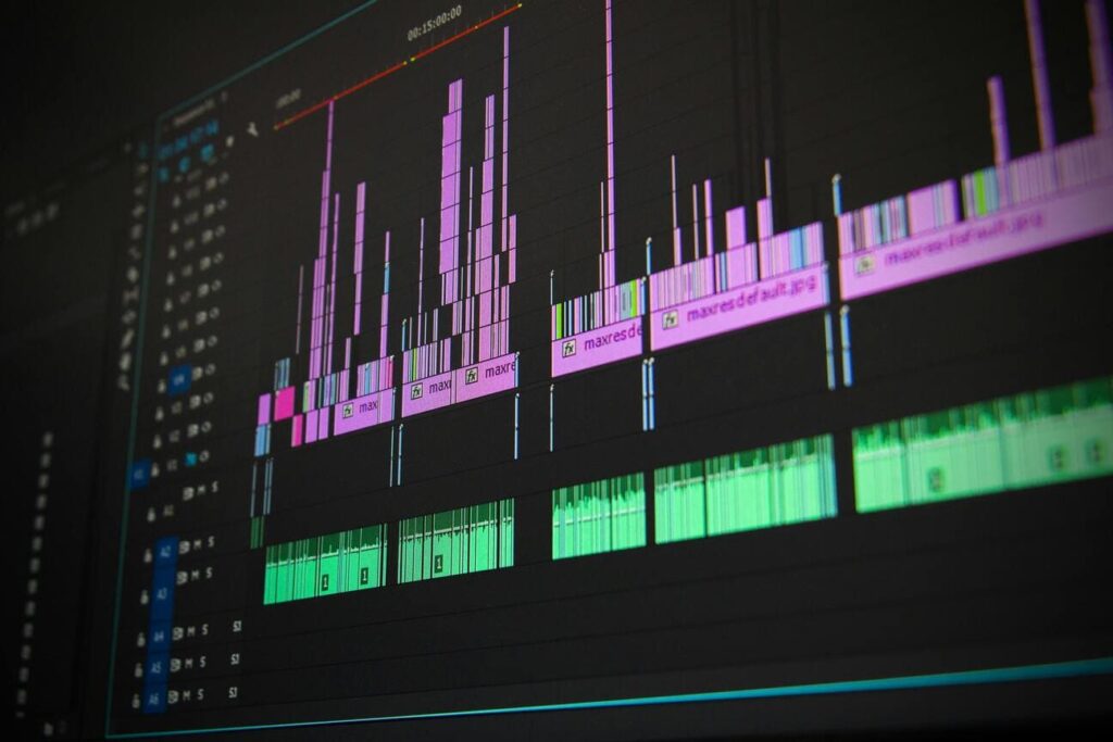 lose-up of a digital audio workstation screen showing a complex audio editing timeline with multiple tracks in various colors, including prominent vertical bars and waveform displays.